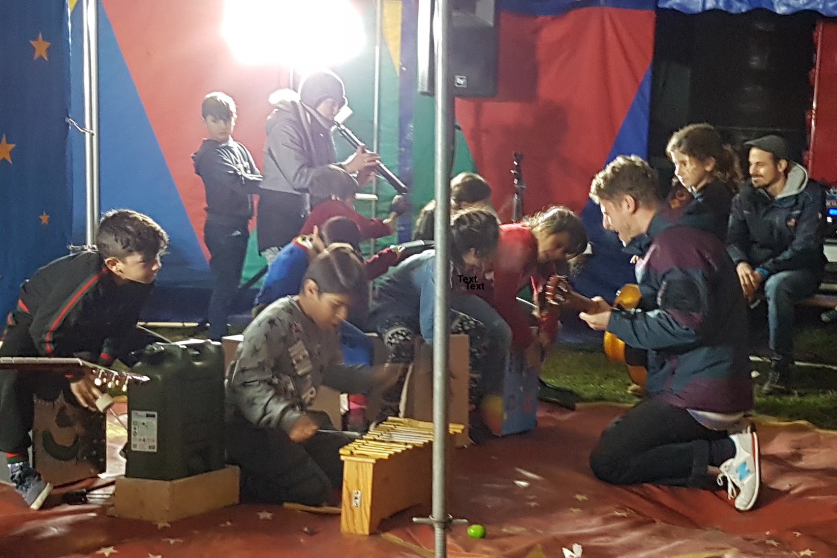 Grundschulkinder spielen mit Dozenten auf dem Boden eines Zeltes energetisch auf Band- und Orff-Instrumenten